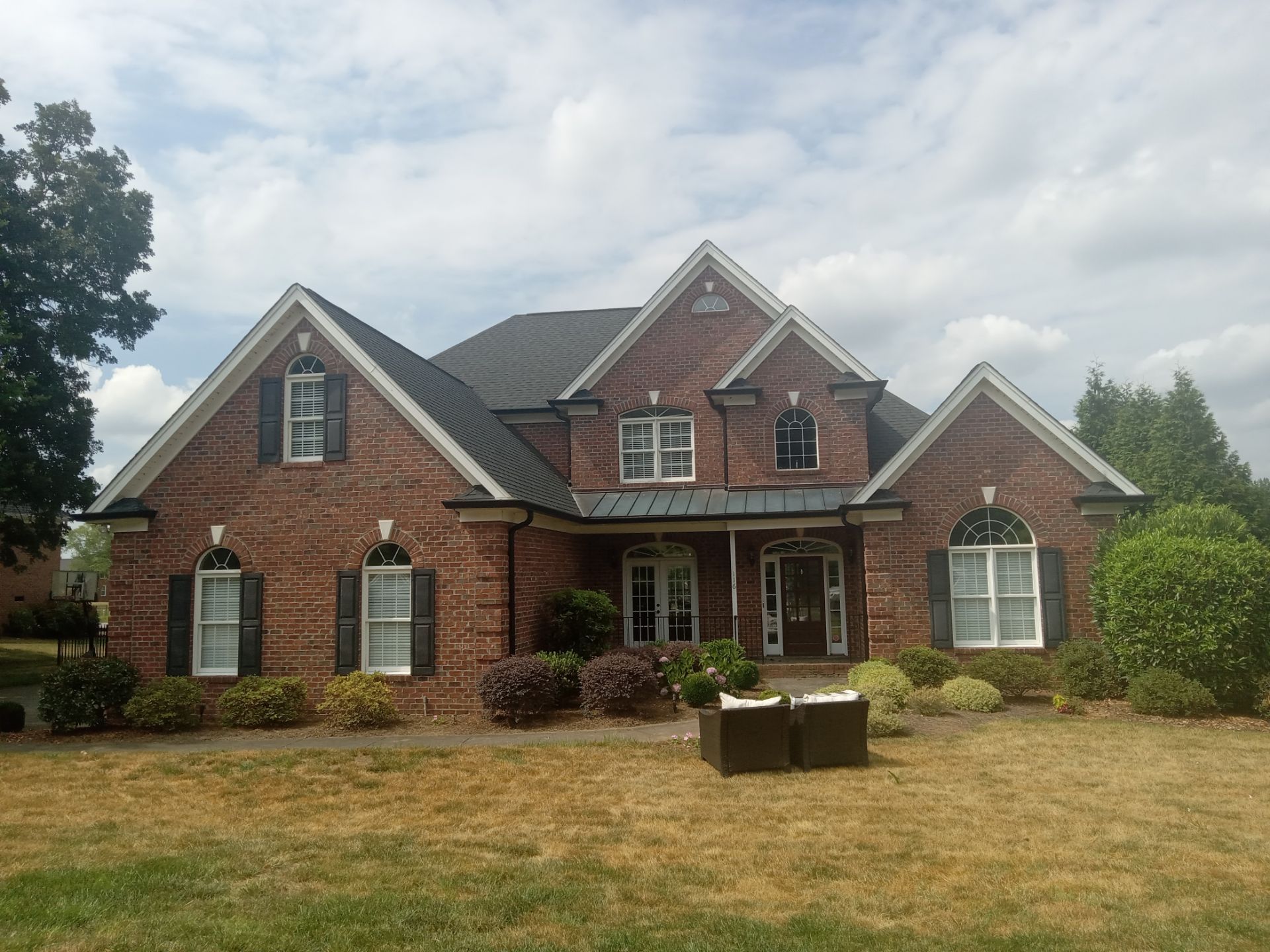 pressure washing brick exterior of a two story red brick house with white trim and black shutters