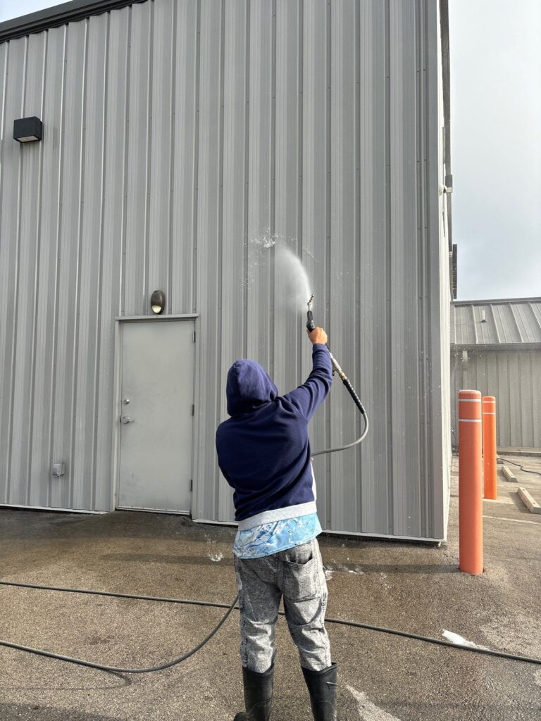 the service shown is cleaning the exterior metal siding of a commercial building using pressure washing techniques